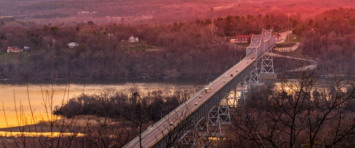 A suspension bridge over a river with mountains in the background.