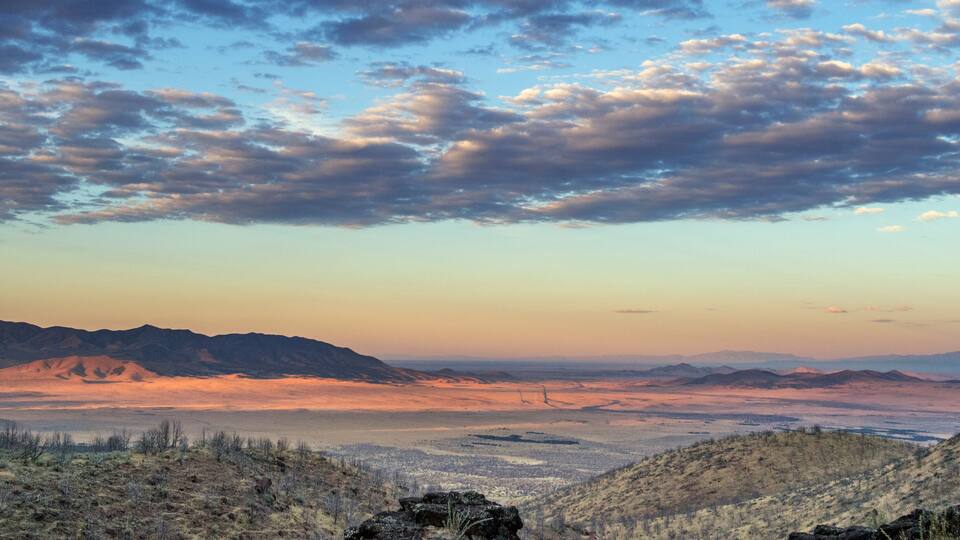 A mountainous landscape with a valley and distant mountains under a partly cloudy sky.