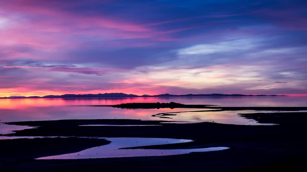 A sunset over a calm lake with a silhouette of mountains in the distance.