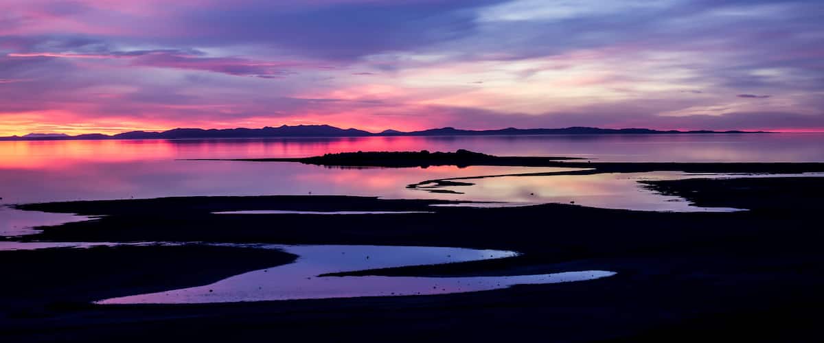 A sunset over a calm lake with a silhouette of mountains in the distance.