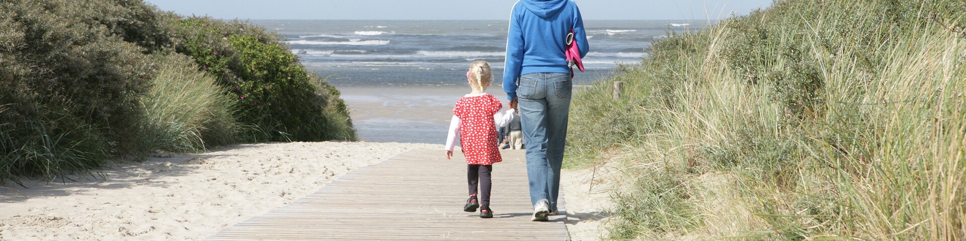 A wooden boardwalk leading to a beach with dunes on either side.