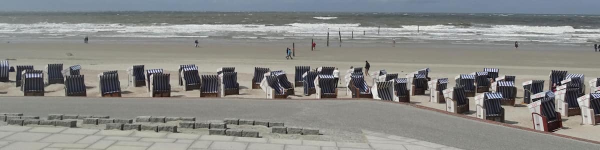 Ein Strand mit Reihen von gestreiften Liegestühlen und einem steinernen Weg, der zum Meer führt.