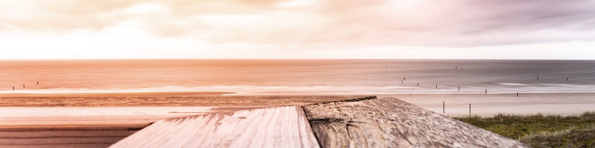 Ein hölzerner Steg führt zu einem Strand unter einem bewölkten Himmel.
