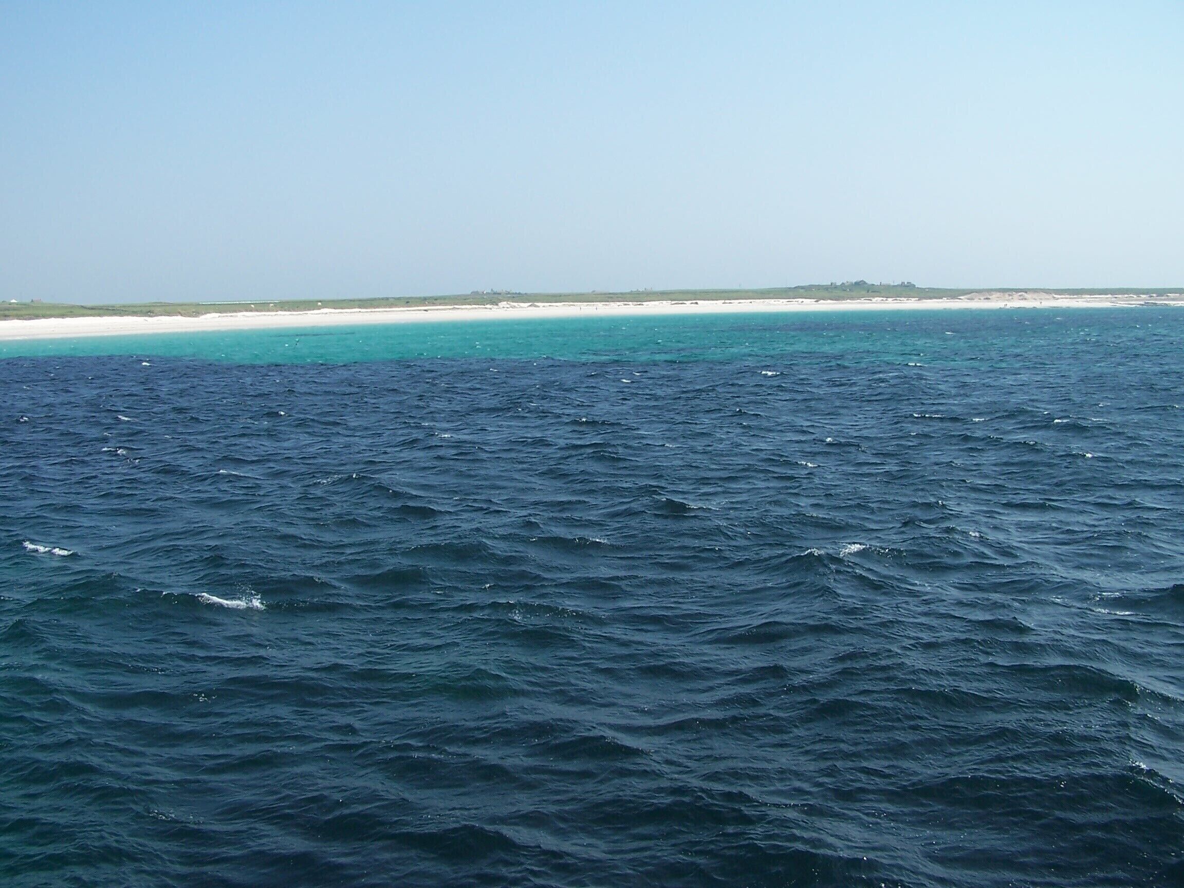 A vast ocean with waves, a sandy beach, and a distant shoreline.