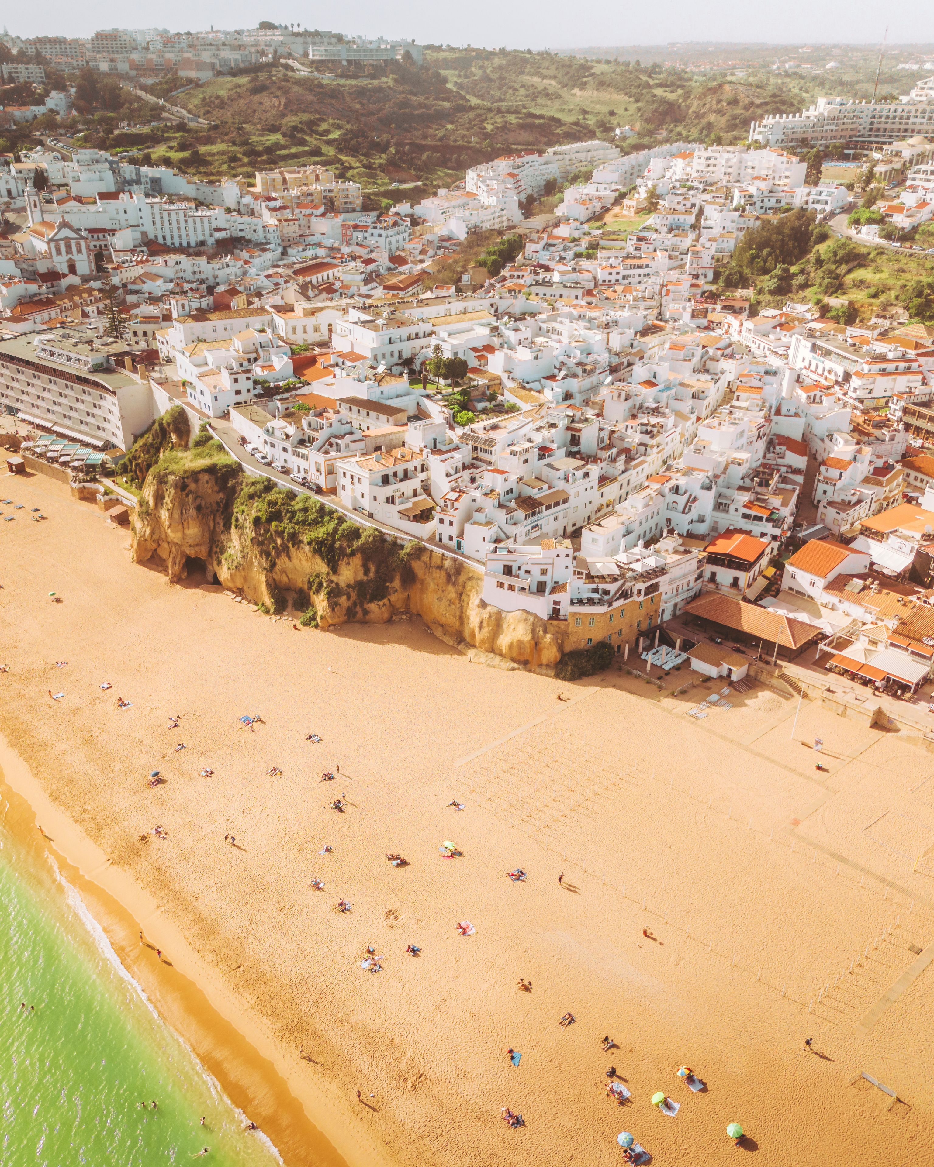 Un pueblo costero con edificios blancos, una playa arenosa y un acantilado con vistas al mar.