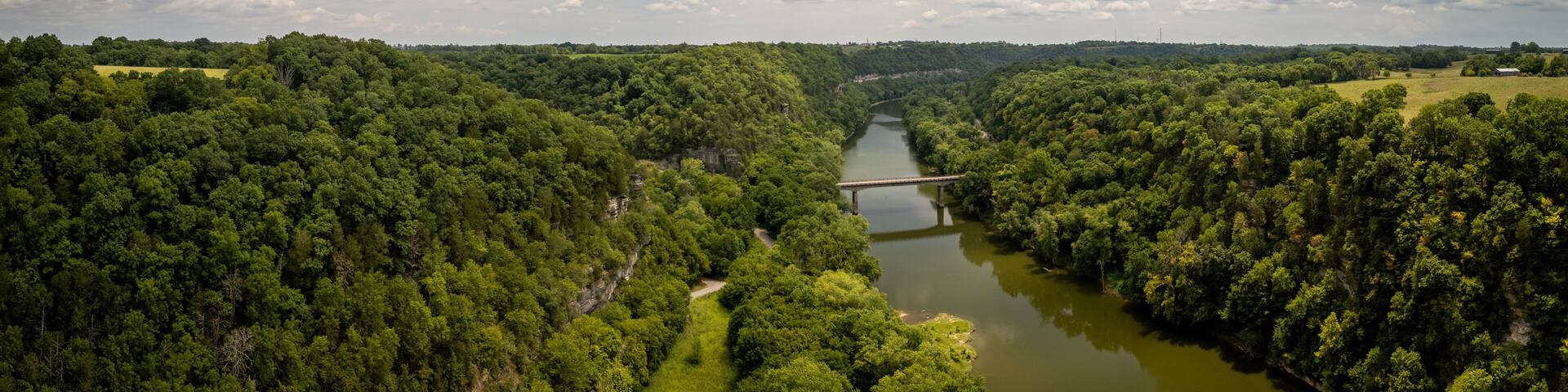 Aerial view of the bridge over the Kentucky River on the road between Harrodsburg and Lexington, showcasing a forest-covered valley surrounded by agricultural fields in Central Kentucky.