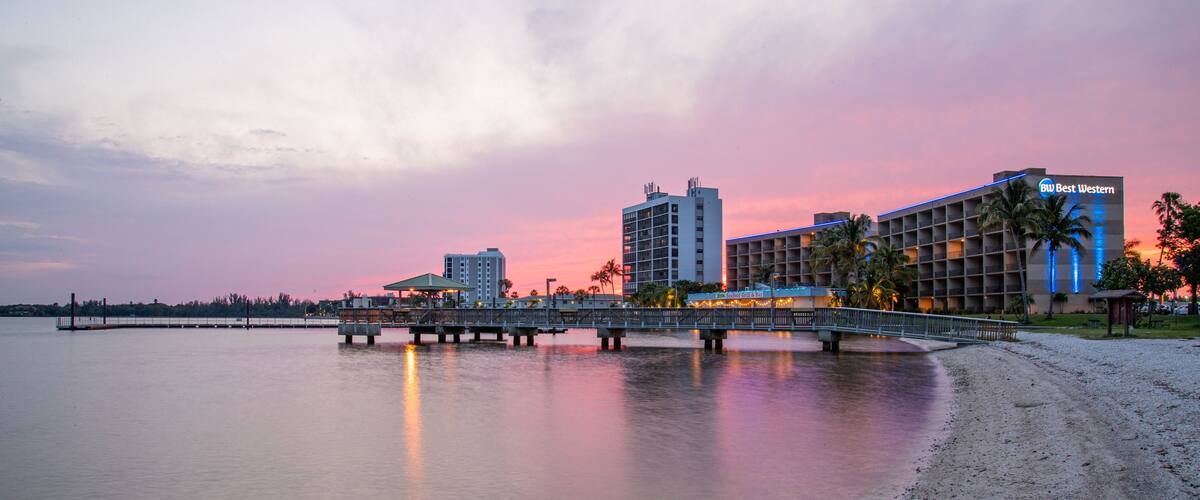 A waterfront with a bridge, buildings, and a beach at sunset.