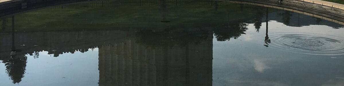 A large historic building with twin towers, a well-maintained lawn, and a reflective pool.