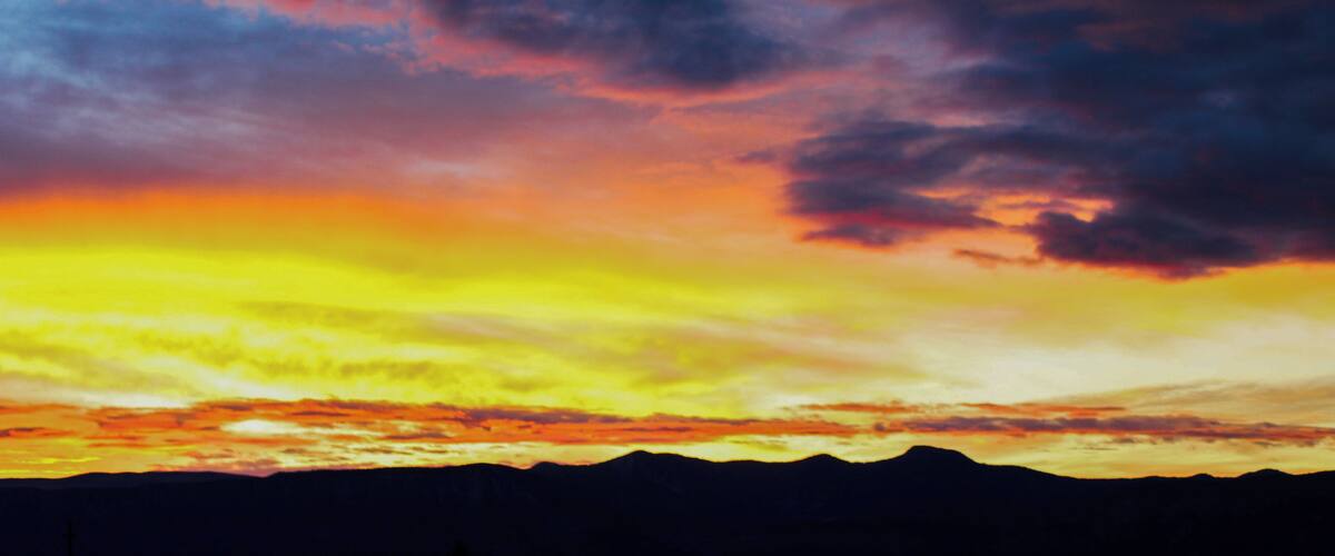 A sunset with a mountain range silhouetted against a colorful sky.