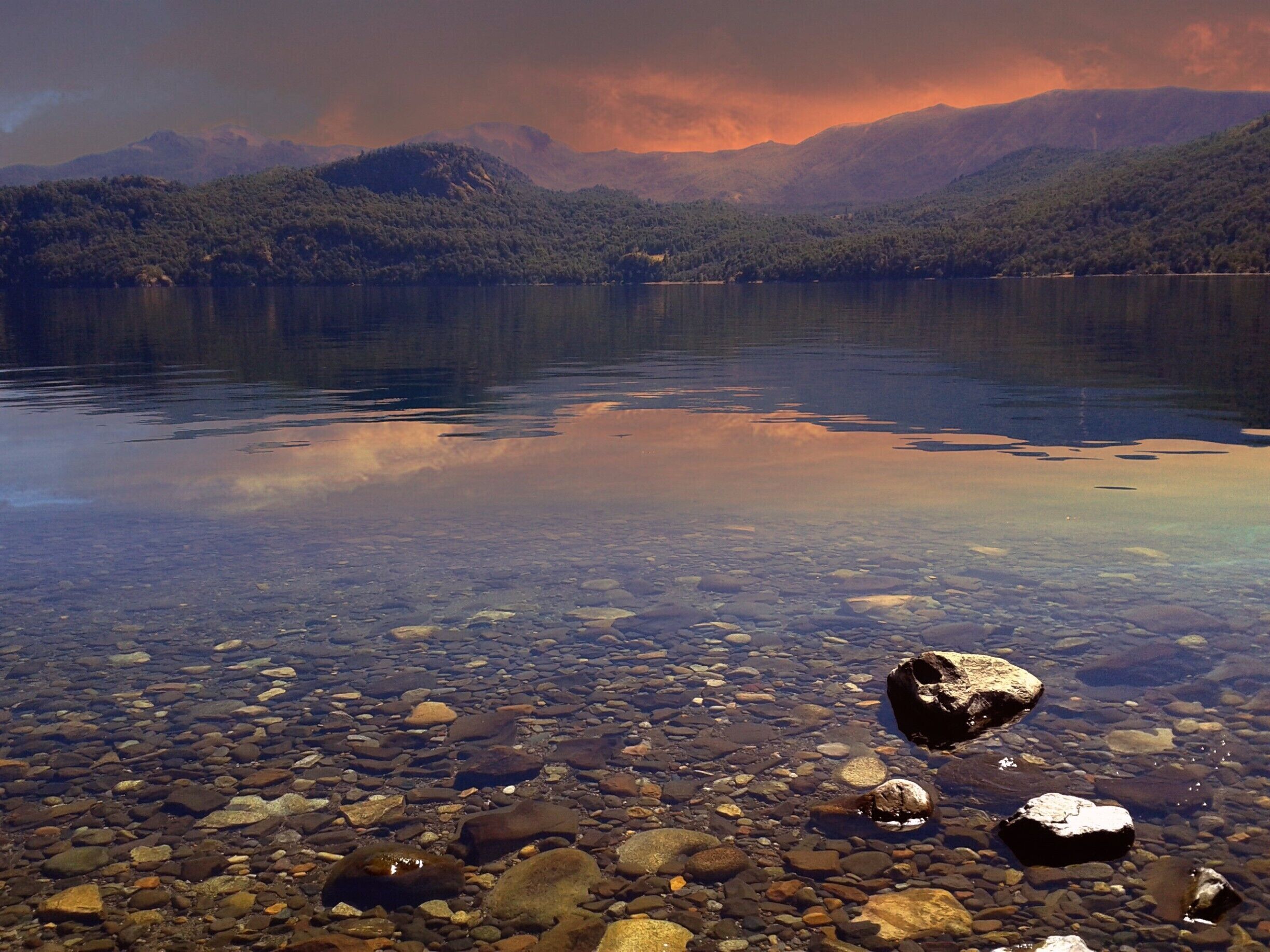 A clear lake with visible rocks and mountains in the background.
