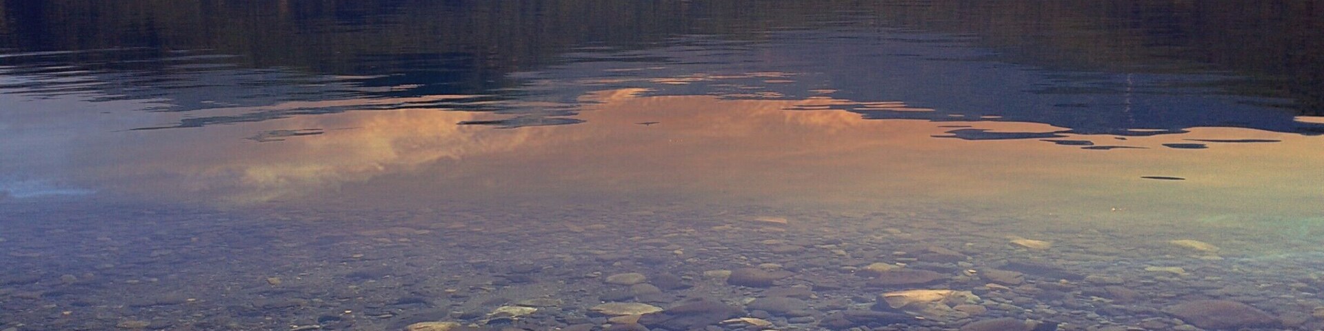 Um lago límpido com rochas visíveis e montanhas ao fundo.