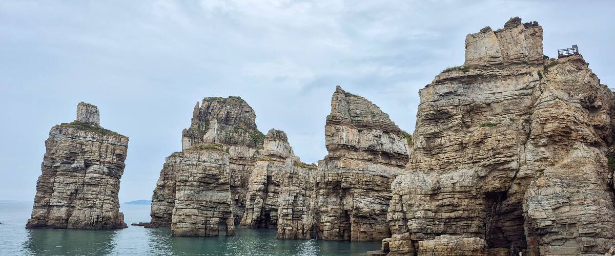 A coastal rock formation with layered cliffs and a small platform on the highest peak.