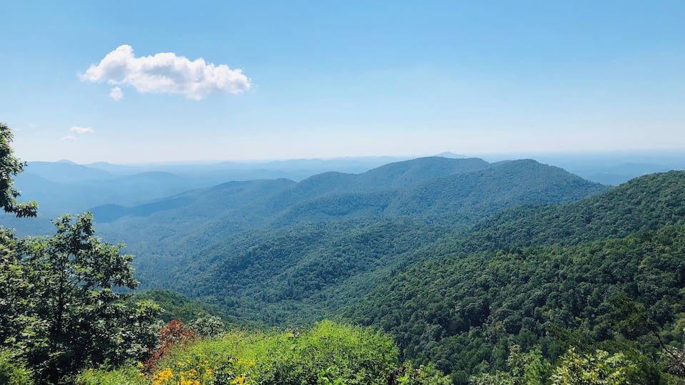 A mountainous landscape with dense green forests and a clear blue sky.