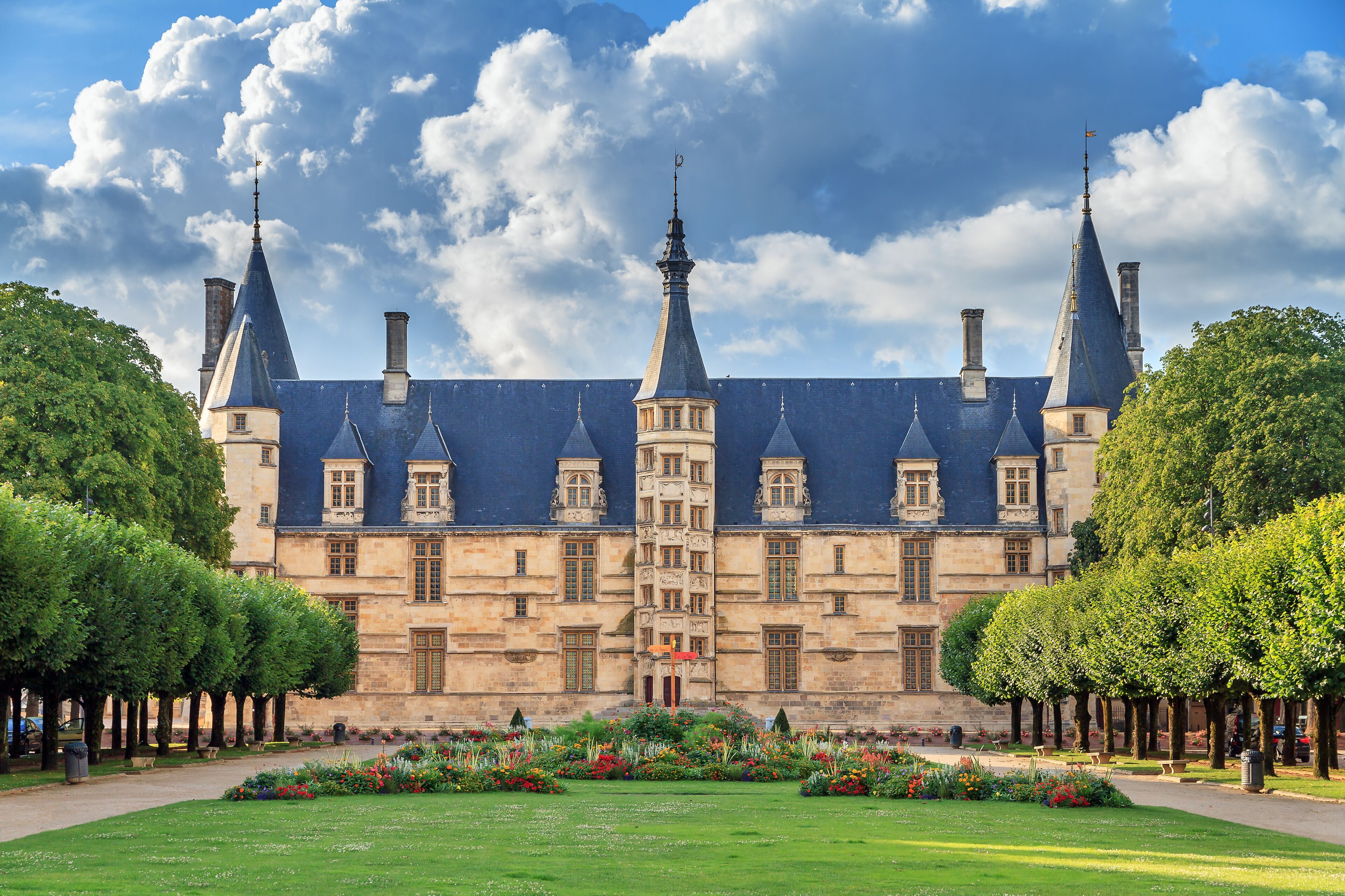 Un bâtiment historique doté de nombreuses flèches, un jardin bien entretenu et un ciel dégagé.
