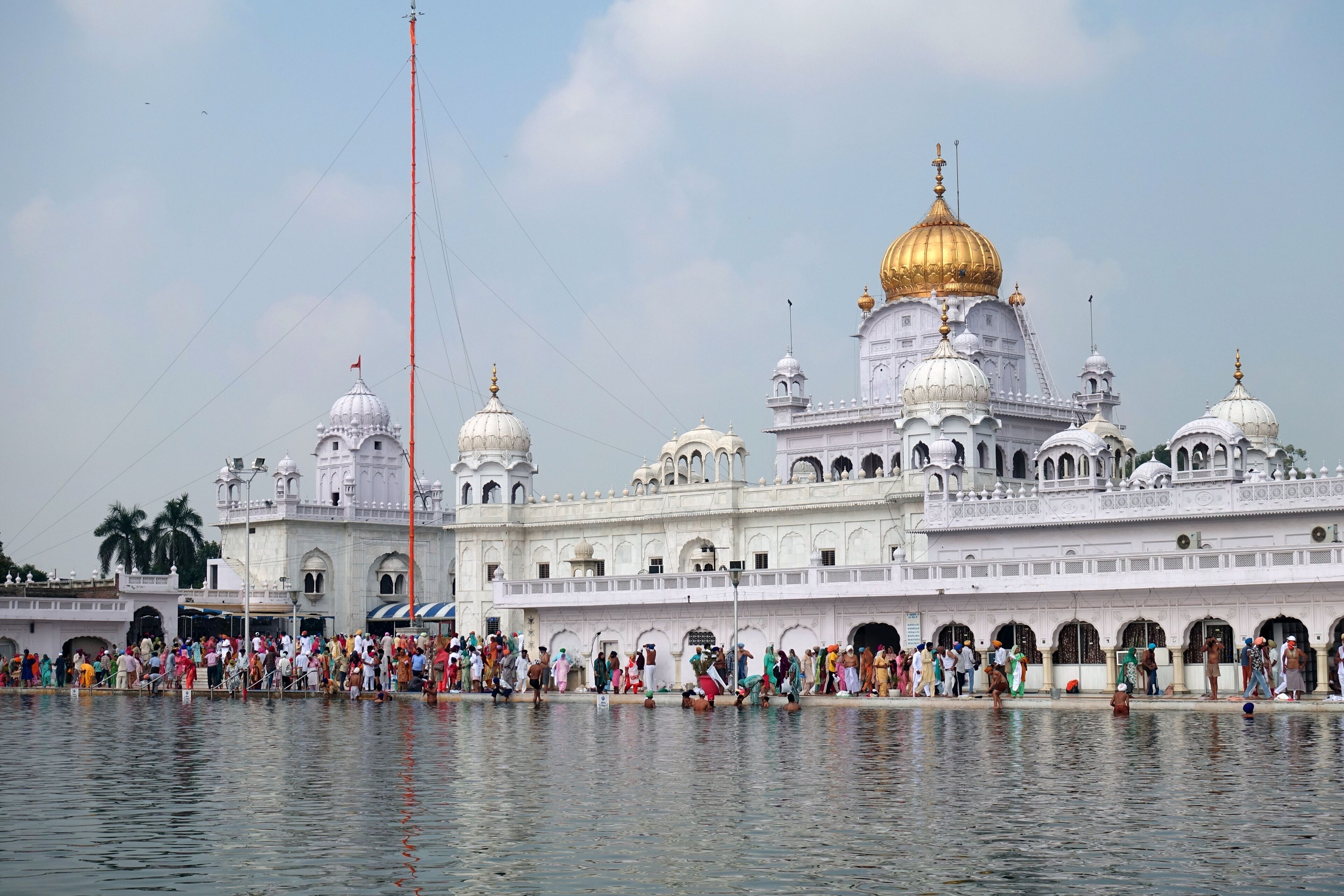 A large white building with golden domes and a crowd by the water.