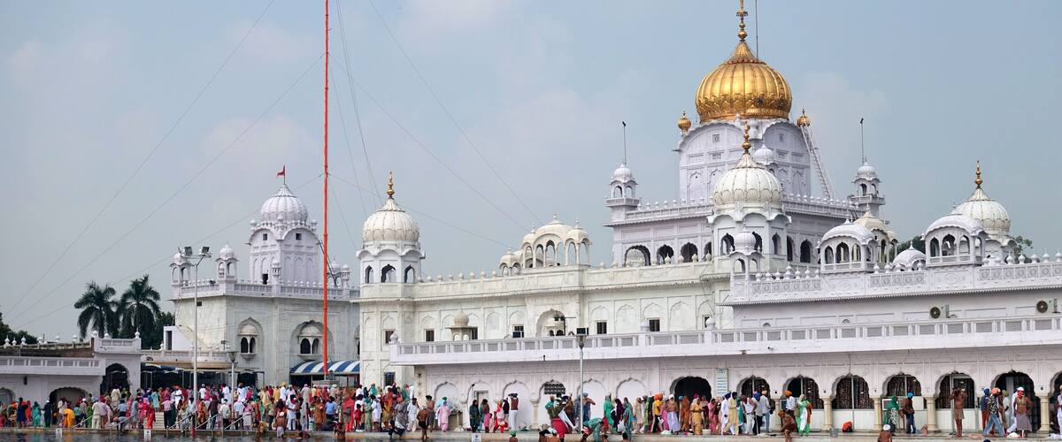 A large white building with golden domes and a crowd by the water.