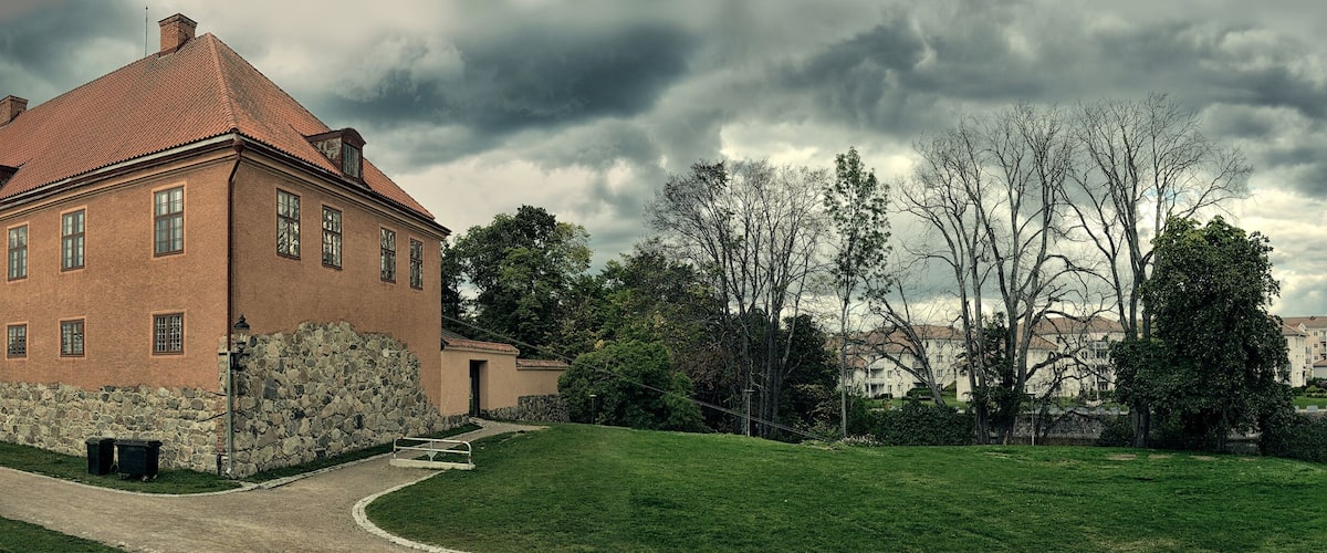 A large brick building with a red roof, surrounded by green grass and trees.