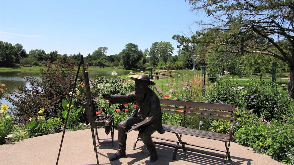 A statue of a man painting on a canvas, a bench, and a pond in a park.