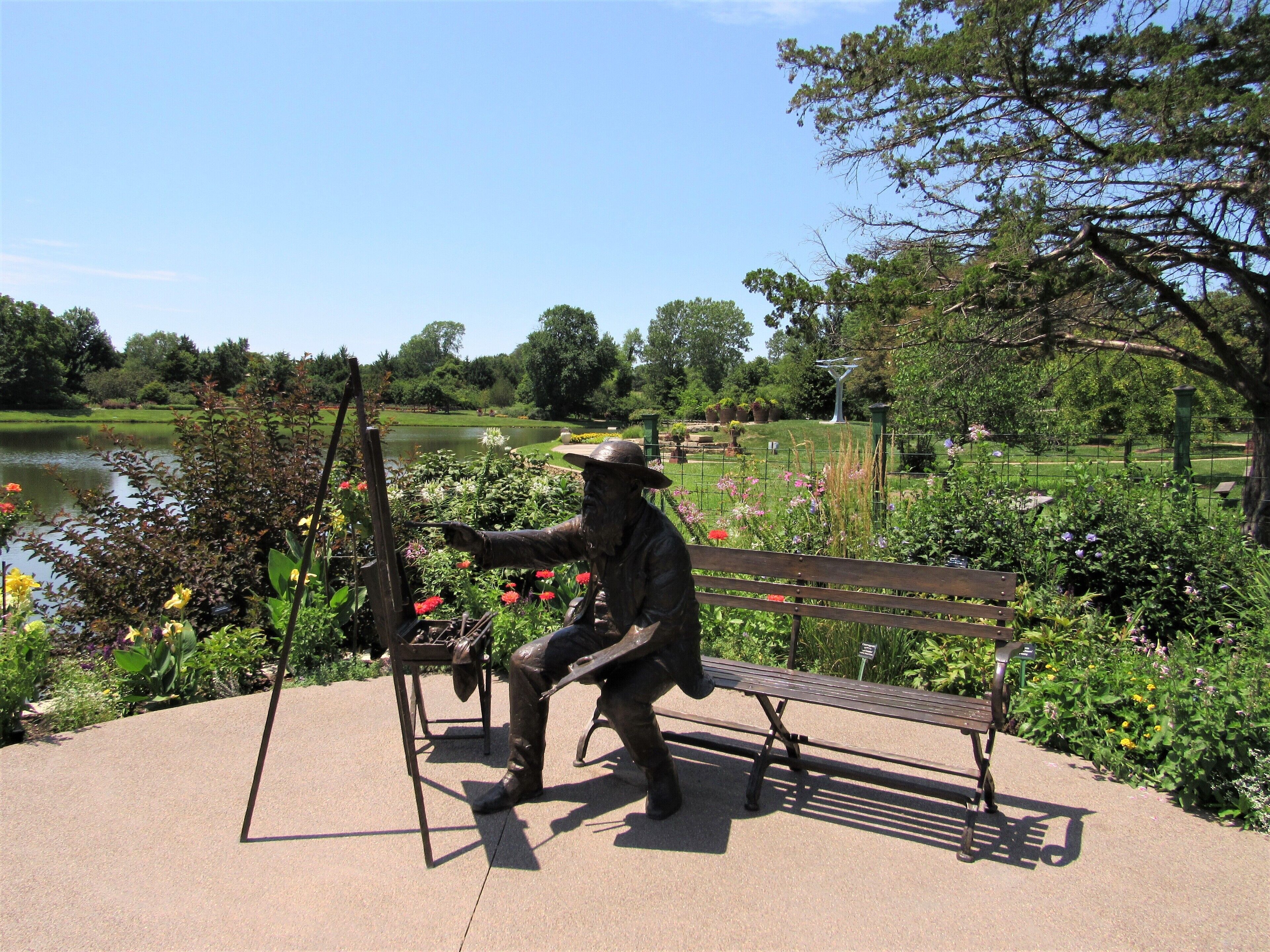 A statue of a man painting on a canvas, a bench, and a pond in a park.
