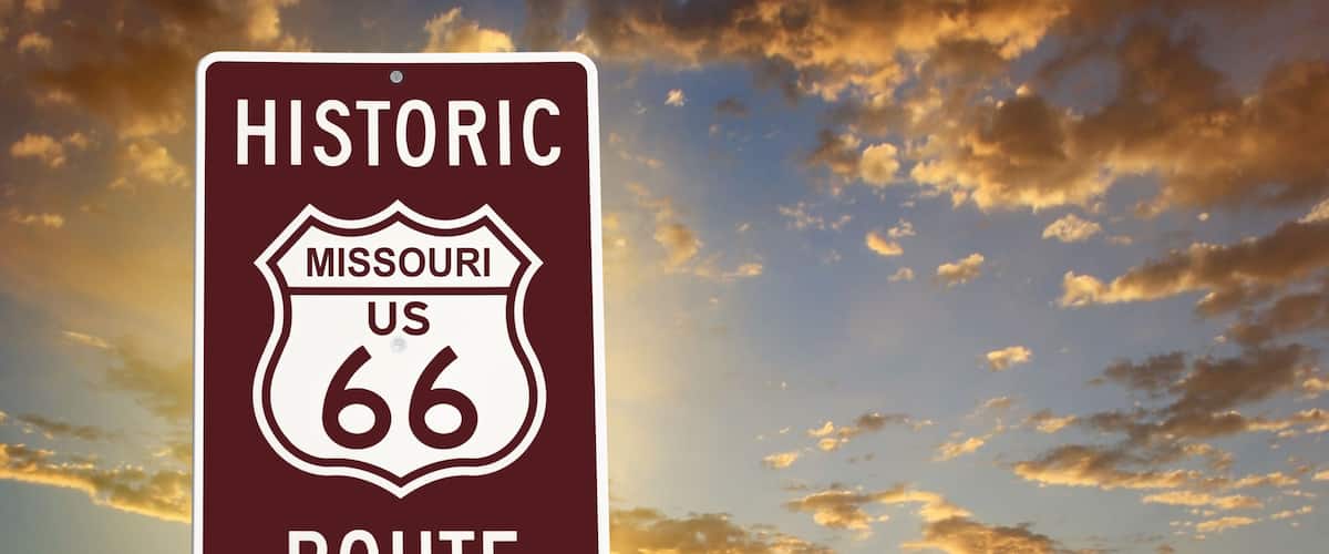 A historic Missouri US 66 route sign against a sunset sky.