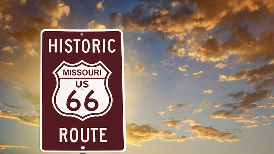 A historic Missouri US 66 route sign against a sunset sky.