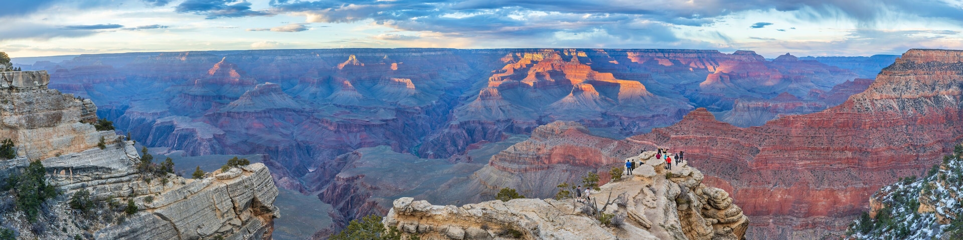 A vast canyon with layered rock formations and a group of people standing on a cliff edge.