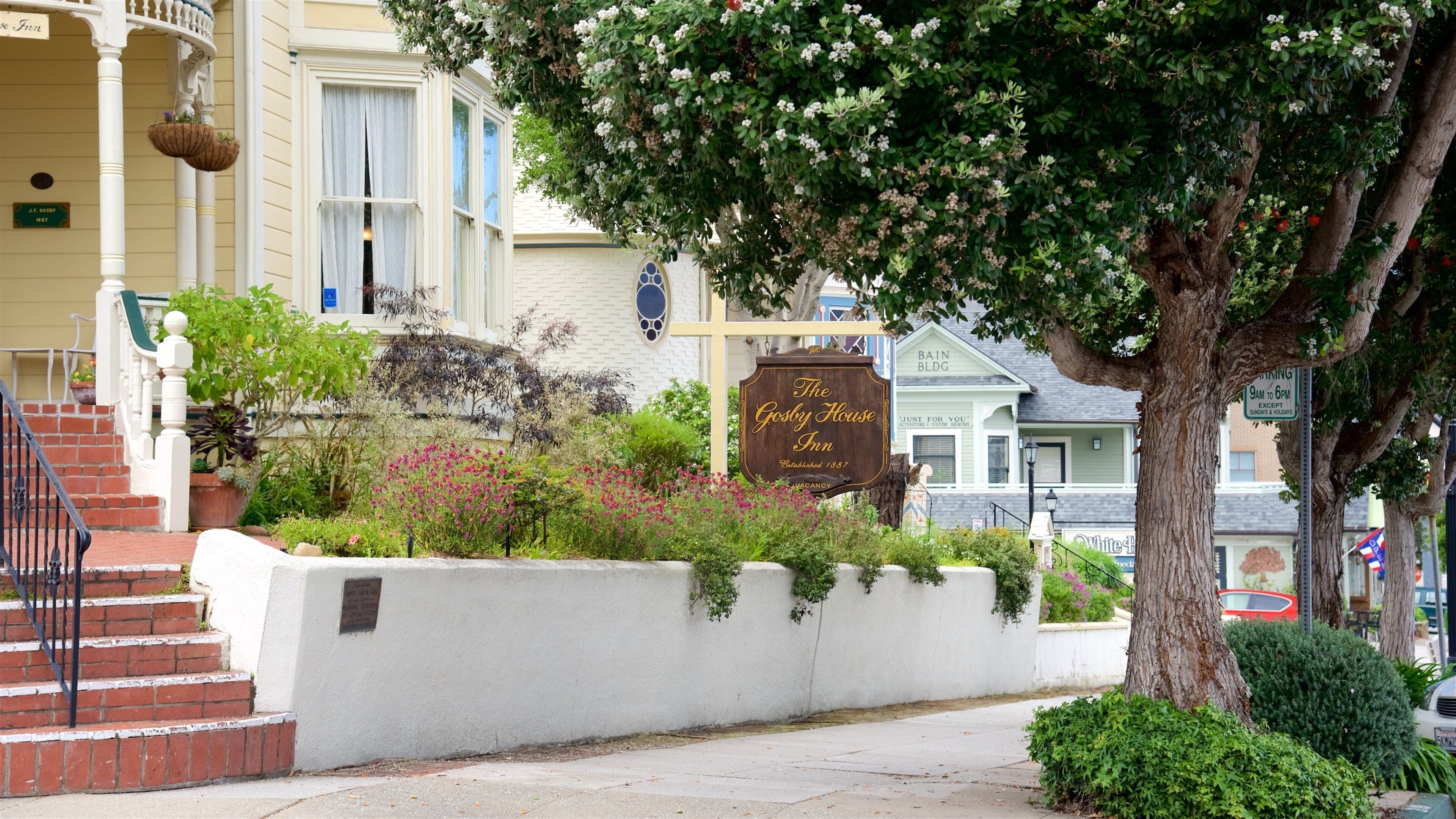 A street with a white building, a sign for The Gosby House Inn, and a tree with pink flowers.