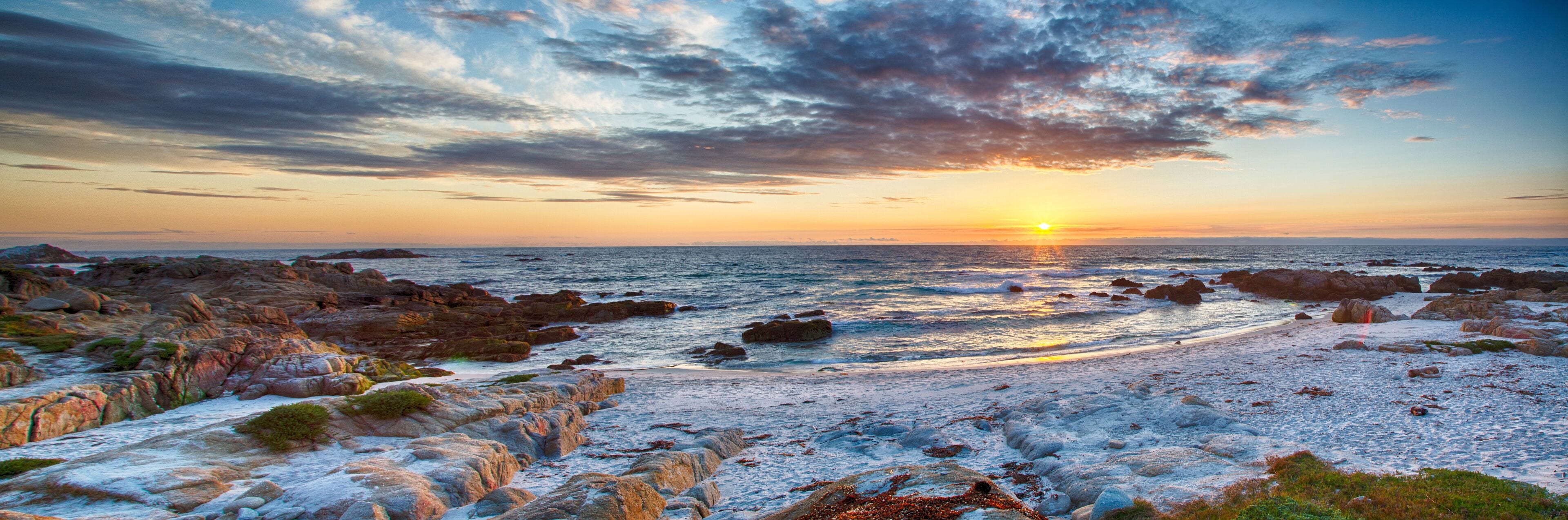 Una costa rocosa con el sol poniéndose sobre el océano.