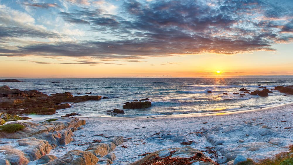 A rocky shoreline with the sun setting over the ocean.