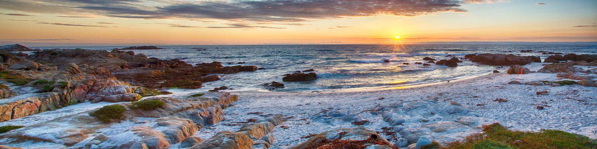 A rocky shoreline with the sun setting over the ocean.