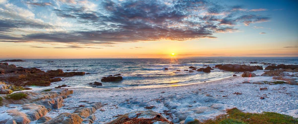 A rocky shoreline with the sun setting over the ocean.
