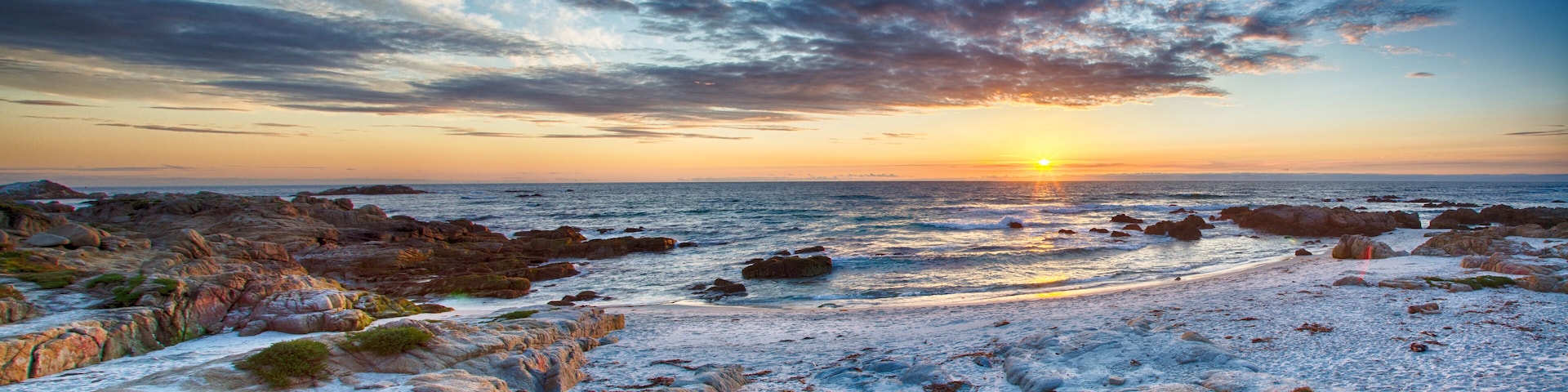 A rocky shoreline with the sun setting over the ocean.