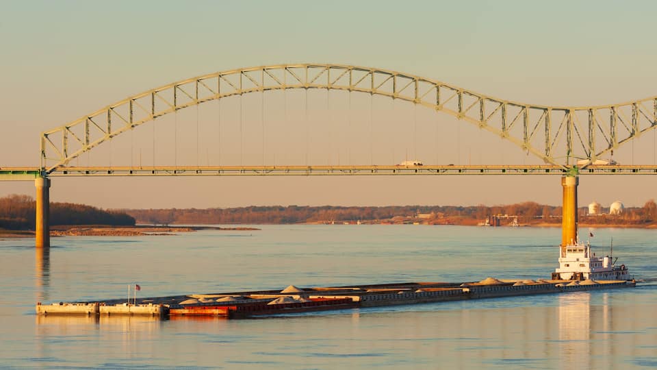 A large bridge spanning a river with a tugboat docked at the base.