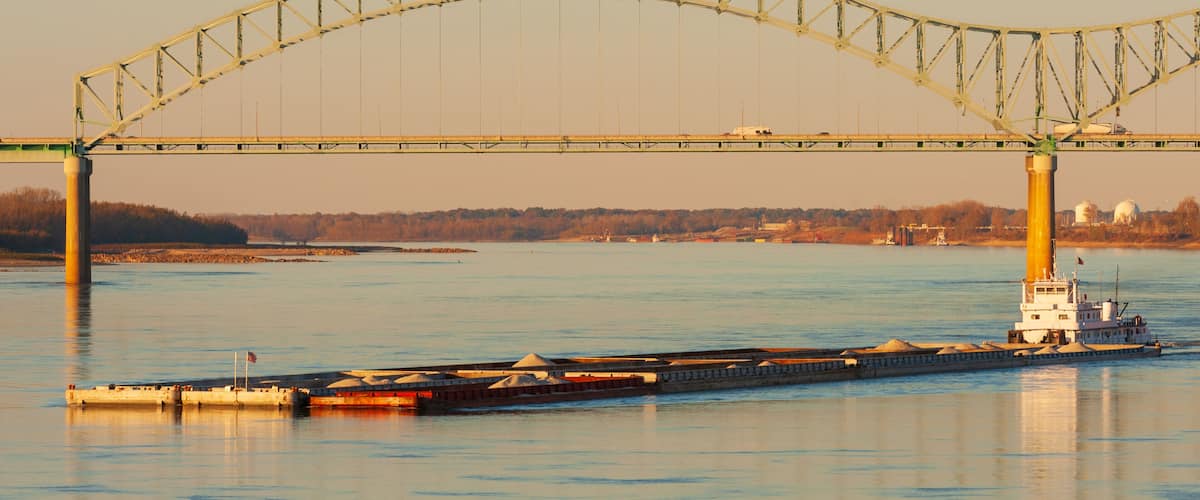 A large bridge spanning a river with a tugboat docked at the base.