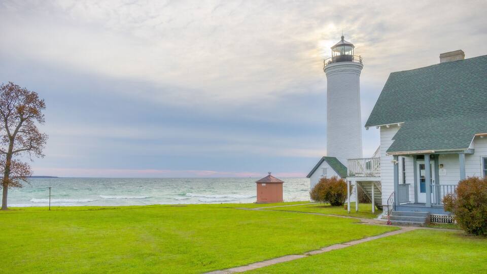 A lighthouse, a grassy area, a building, and a body of water.