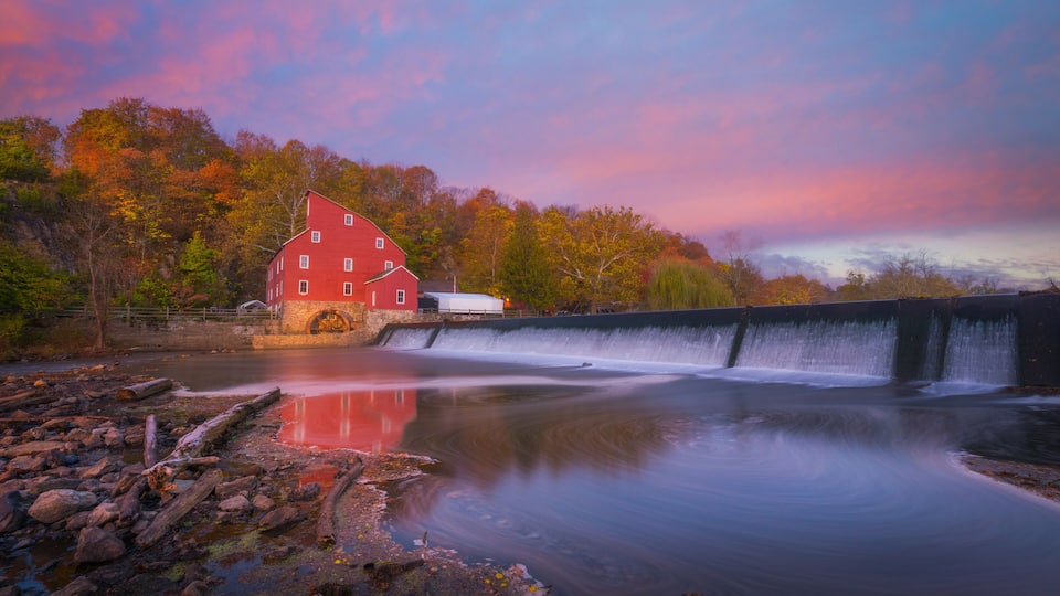 A red building by a waterfall, autumn trees, and a calm river.