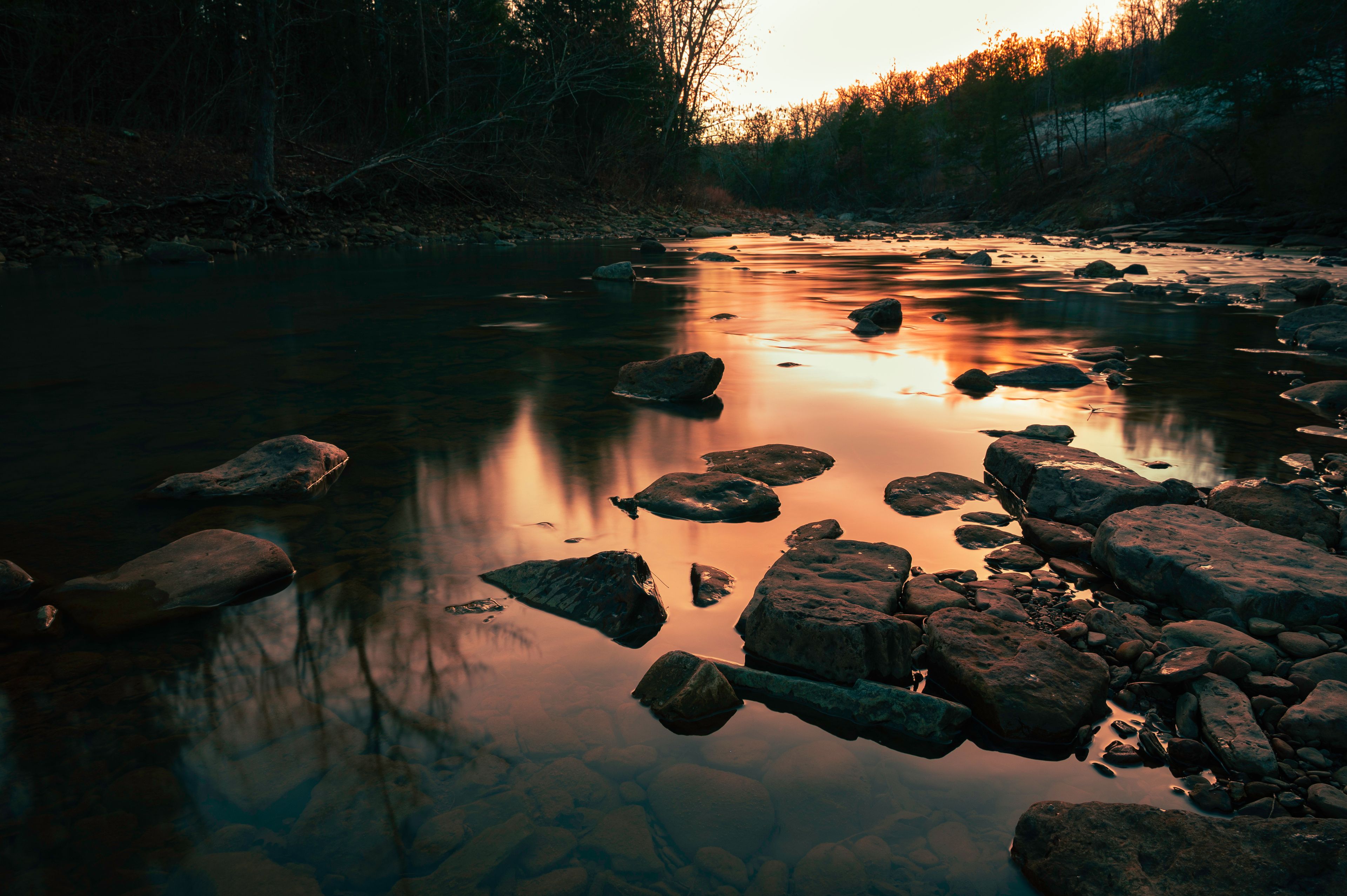 Un fiume con rocce e alberi al tramonto.