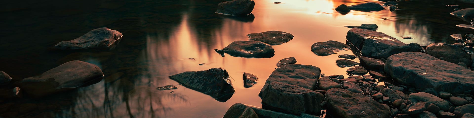 A river with rocks and trees at sunset.