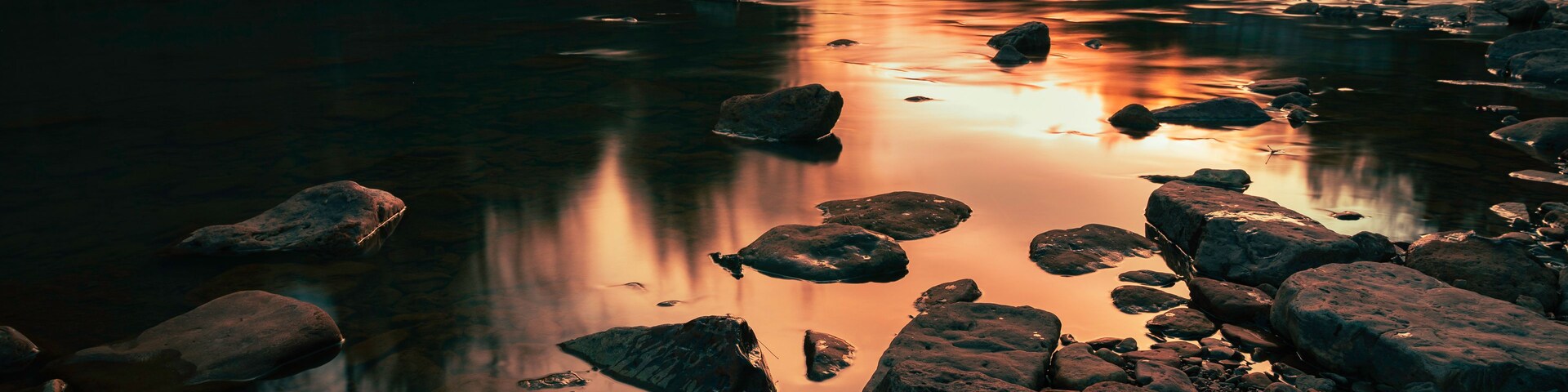Un río con rocas y árboles al atardecer.