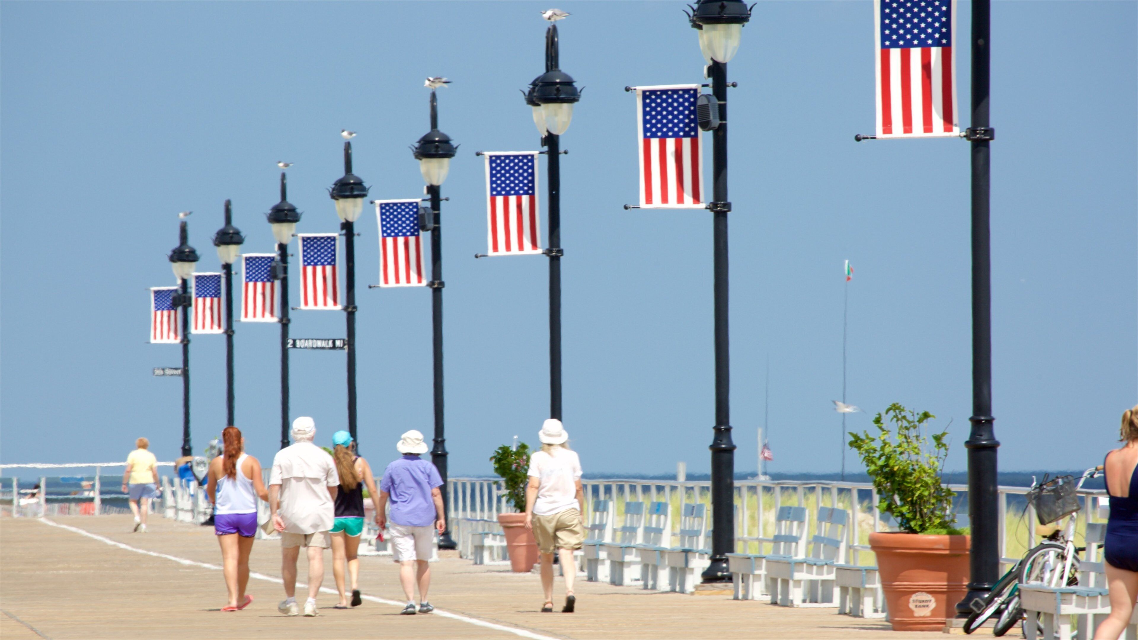 A boardwalk with American flags and street lamps.