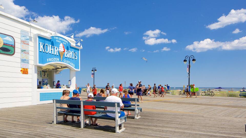 A boardwalk with a frozen food kiosk, benches, and people walking.