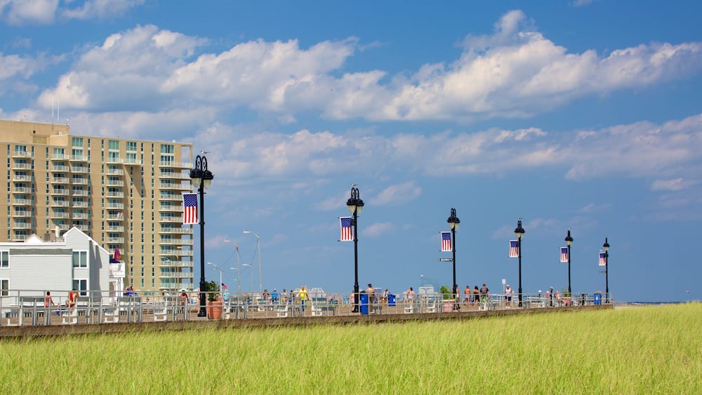 A coastal promenade with American flags, a boardwalk, and a high-rise building.