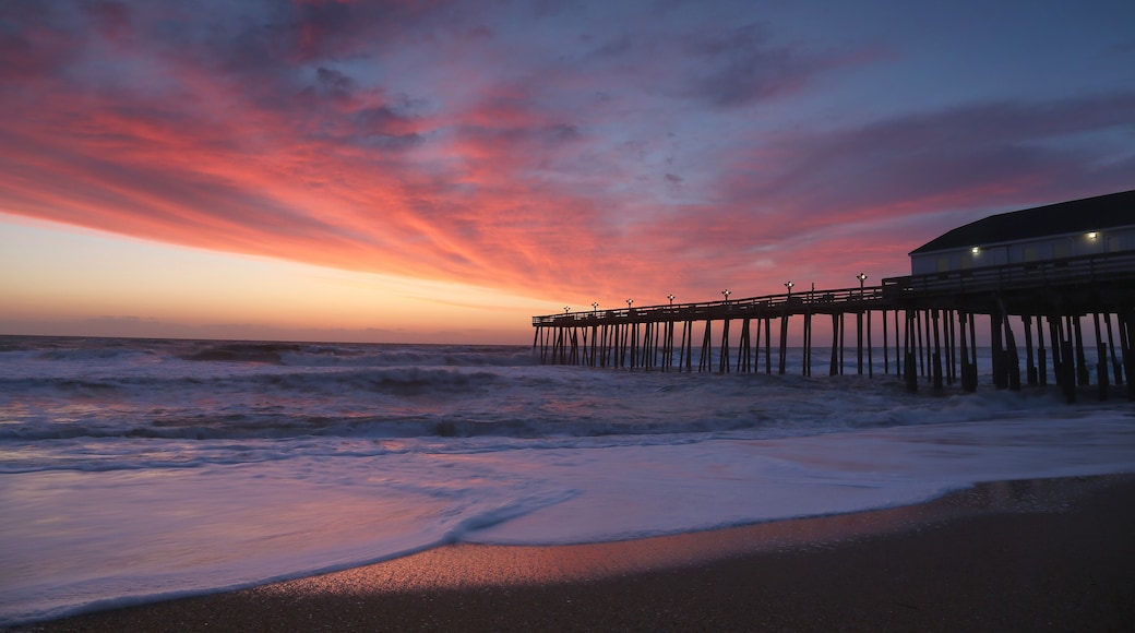 The rising sun visible through pier supports and is reflected in waves by the Nags Head fishing pier on the outer banks of North Carolina