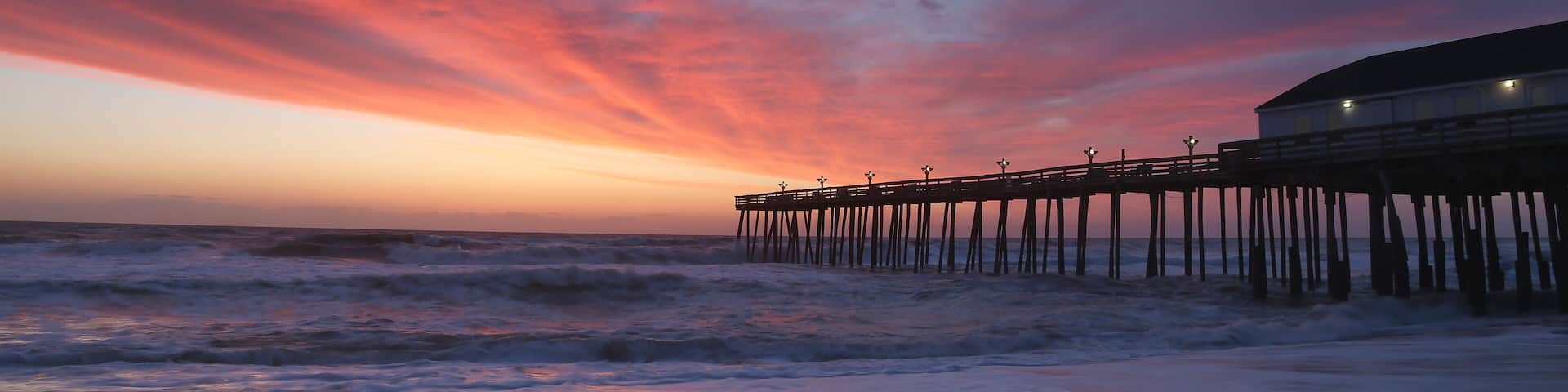 The rising sun visible through pier supports and is reflected in waves by the Nags Head fishing pier on the outer banks of North Carolina