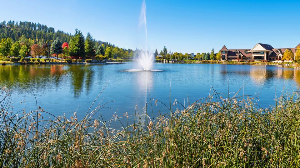 A large water fountain feature in the center of a small lake in the residential and commercial development and park in downtown Coeur d'Alene, Idaho USA.