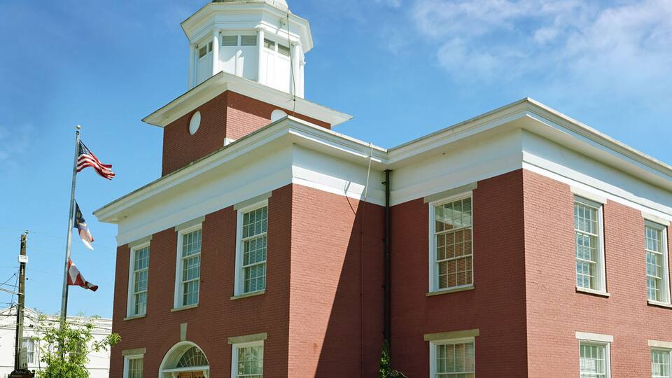 A red brick building with a white tower, a flag, and a sign.