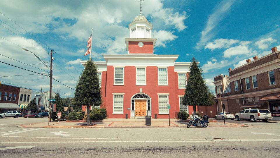 A red brick building with a white dome and a flagpole with flags.