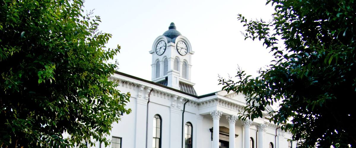 A white building with a clock tower, surrounded by a garden of red and white flowers.