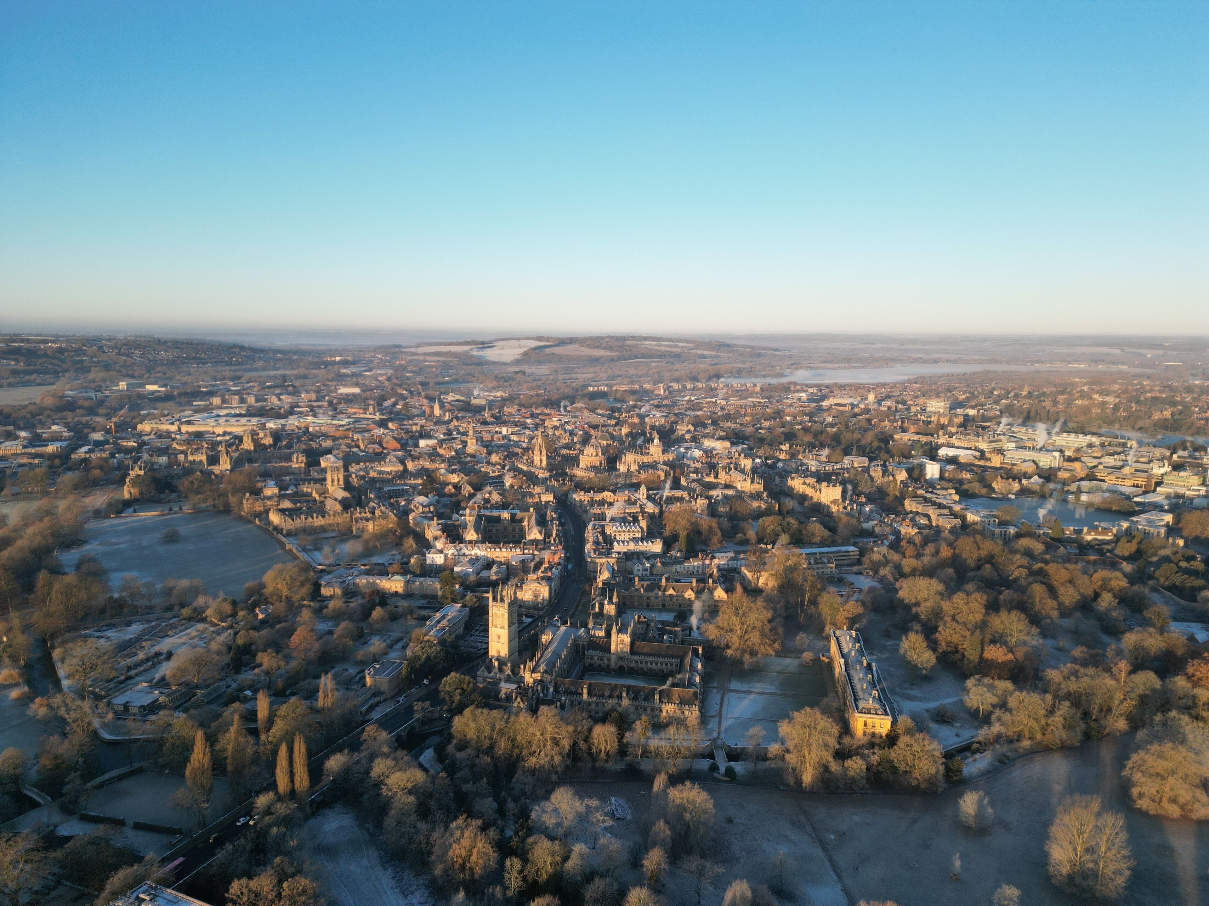 An aerial view of a historic city with dense architecture, a prominent cathedral, and surrounding green spaces.