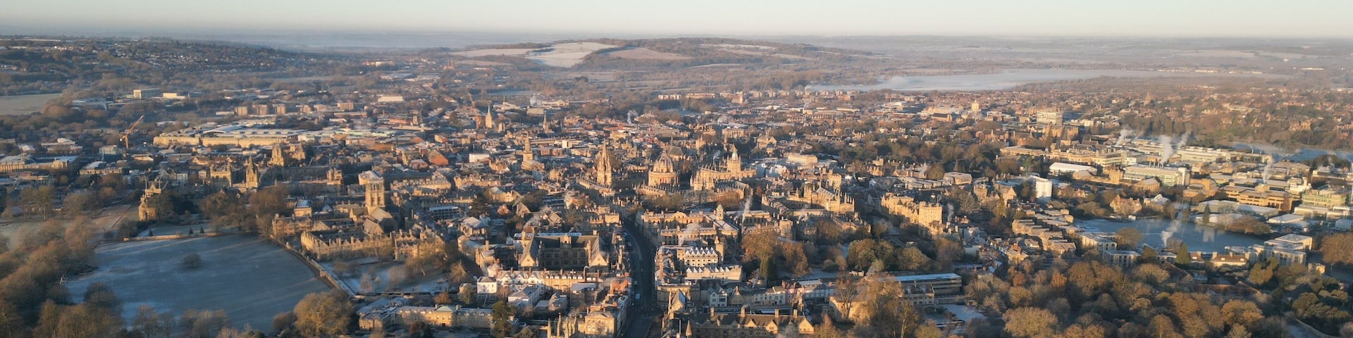 An aerial view of a historic city with dense architecture, a prominent cathedral, and surrounding green spaces.